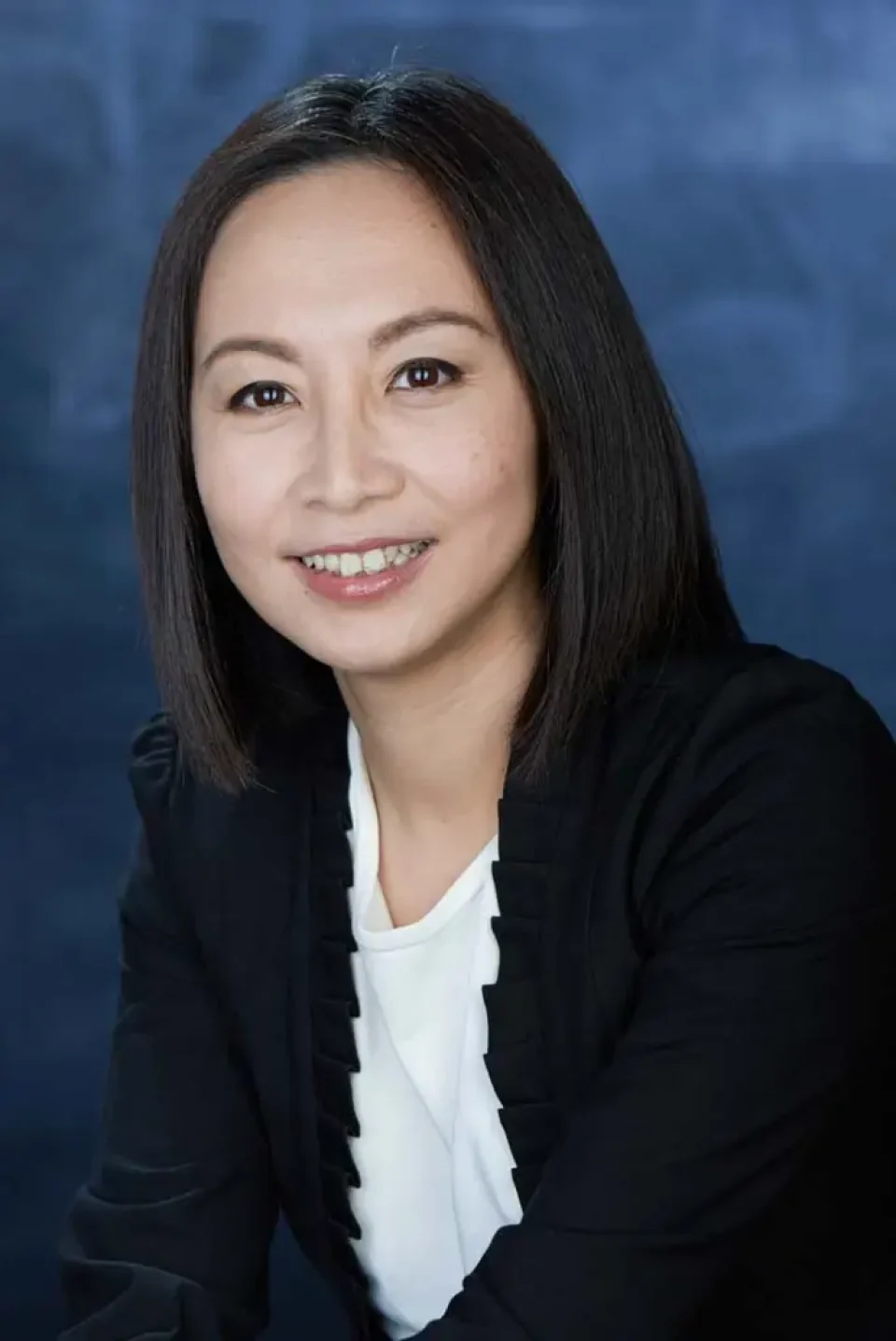 Corporate portrait of a woman in a dark cardigan smiling against a dark background — singapore corporate portrait photography, corporate portrait photographer singapore