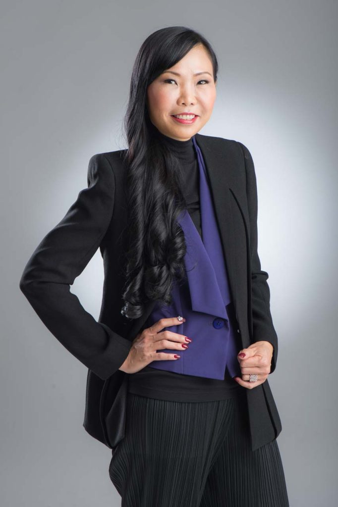 Studio portrait of a woman in a dark jacket over purple, hand raised to her face, against a soft grey background — corporate portrait photographer singapore